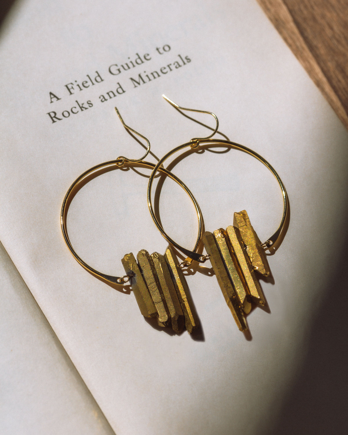 Supernova Earrings in Gold, displayed on a book about rocks and minerals.