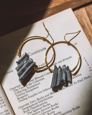 Supernova earrings in black with gold hoops on a book page.