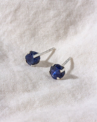 Pair of blue gemstone stud earrings on a white fabric background