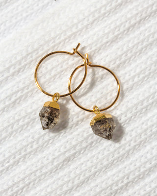 A pair of gold hoop earrings with dangling raw, rough-textured gray Herkimer quartz stones.