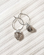 A pair of silver hoop earrings with rough, faceted  Herkimer quartz crystal pendants.