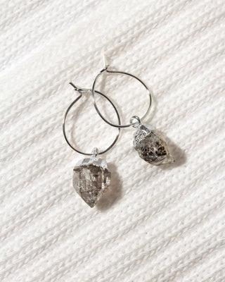 A pair of silver hoop earrings with rough, faceted  Herkimer quartz crystal pendants.