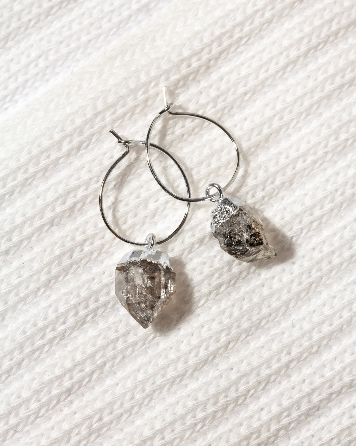 A pair of silver hoop earrings with rough, faceted  Herkimer quartz crystal pendants.