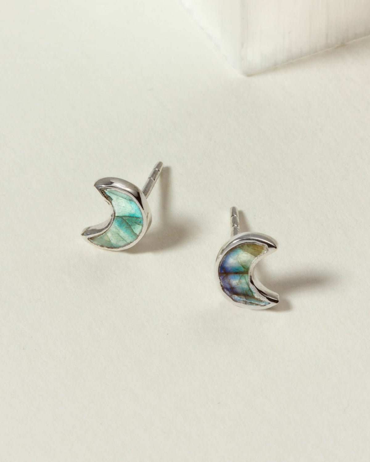 Pair of silver labradorite crescent moon shaped charm earrings on a white surface.