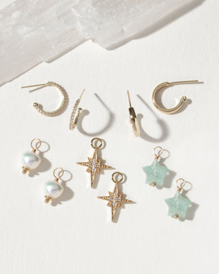 Hoop earring set showing gold hoops, pearl, starburst, and aquamarine star charm pairs.