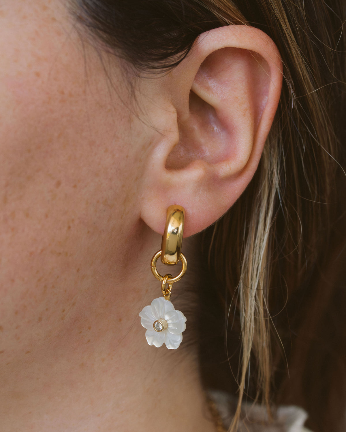 Closeup of woman wearing mother of pearl floral interchangeable huggie hoop earring.