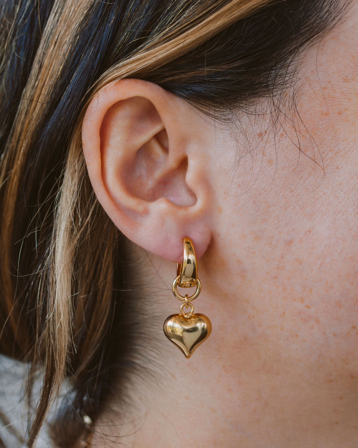 Person wearing gold heart shaped earrings.