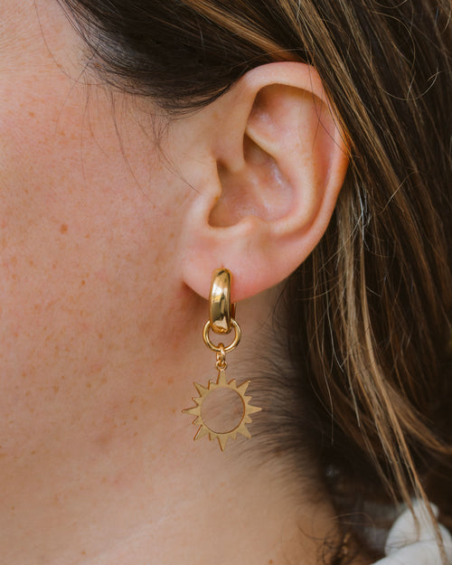 Closeup of woman warring gold plated sun shaped hoop earring.