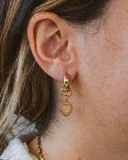 Person wearing gold heart shaped earrings.