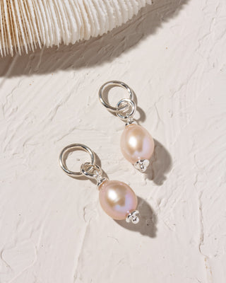 Silver Pearl earring charms on a textured white surface with a shell in the background