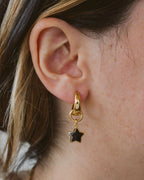 Closeup of person wearing gold hoop earring with black onyx star charm.