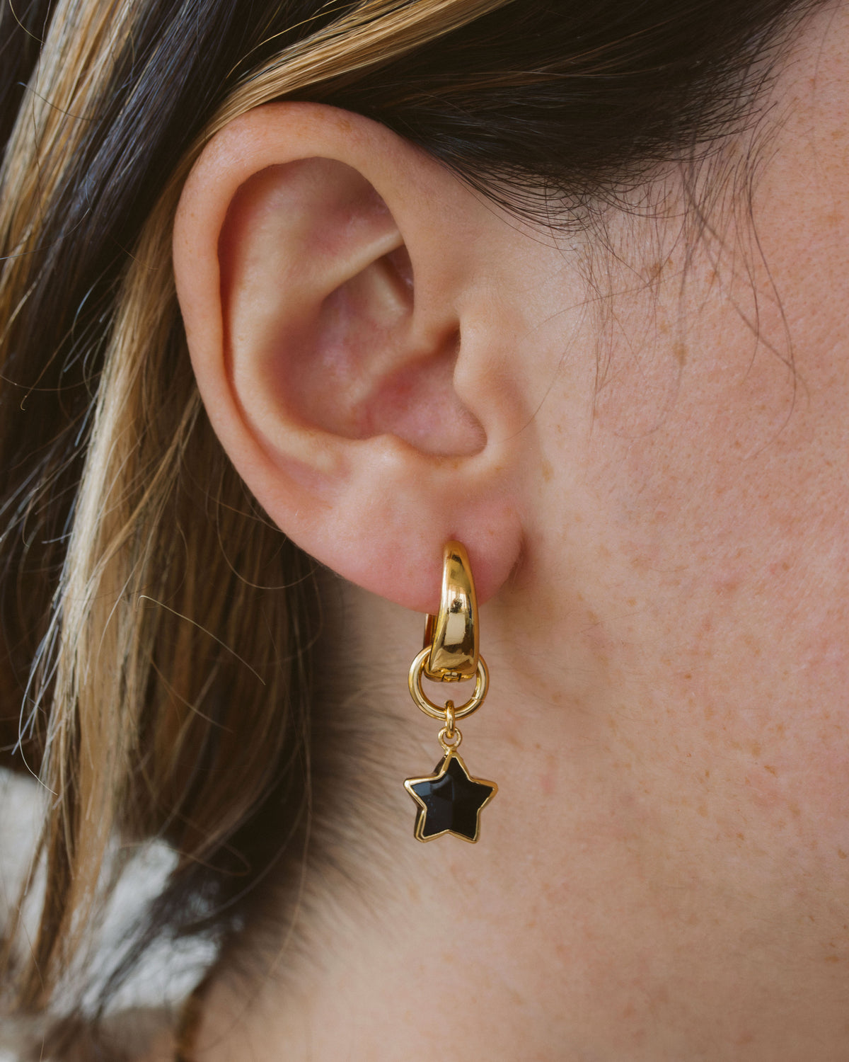 Closeup of person wearing gold hoop earring with black onyx star charm.