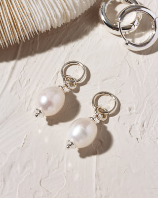 Pearl earring charms on a textured white surface with a coral in the background