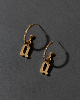 Gold hoop earrings with letter 'a' charms on a dark gray background