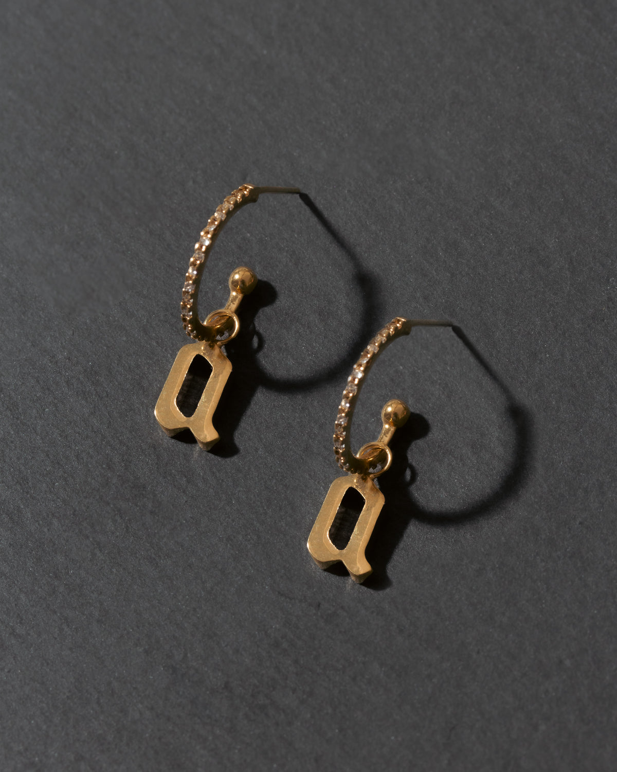 Gold hoop earrings with letter 'a' charms on a dark gray background