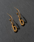 Gold earrings with 'b' charms on a dark gray background
