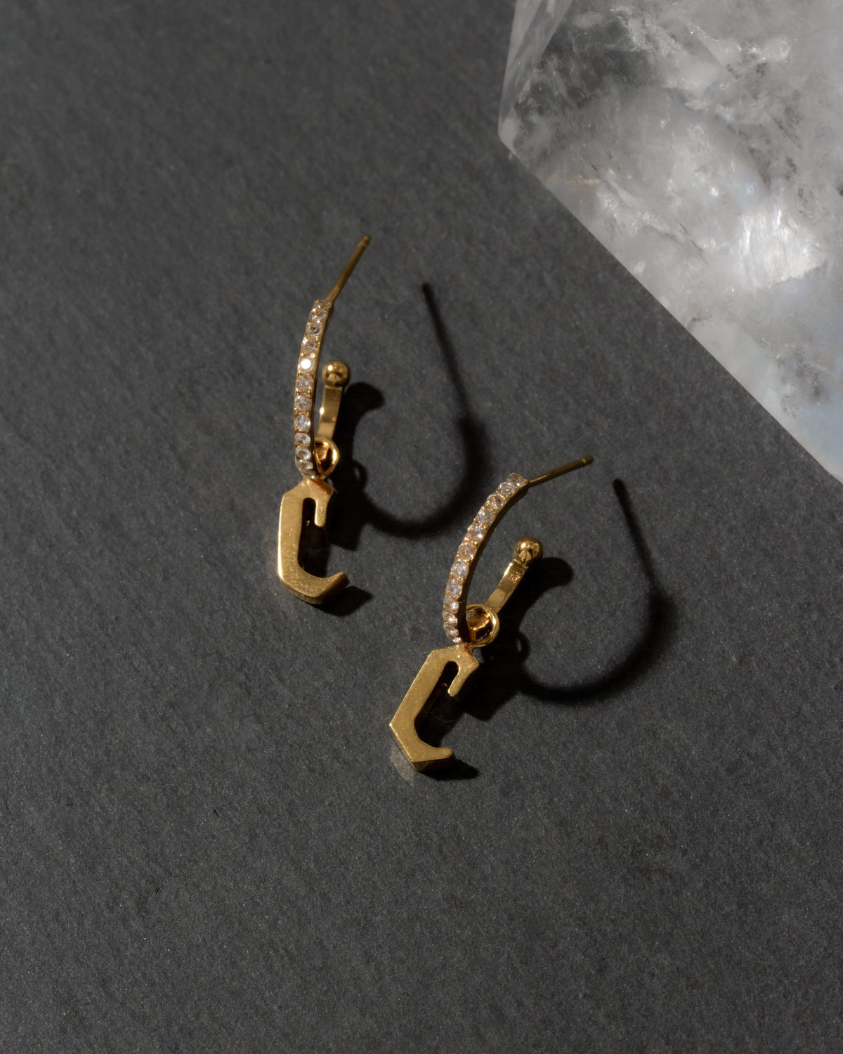 Gold earrings with letter 'C' design on a dark surface