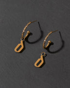 Gold earrings with letter 'd' charm on a dark gray background