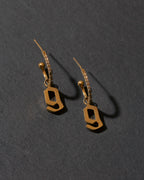 Gold letter 'g' earrings on a dark gray background