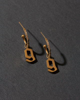 Gold letter 'g' earrings on a dark gray background