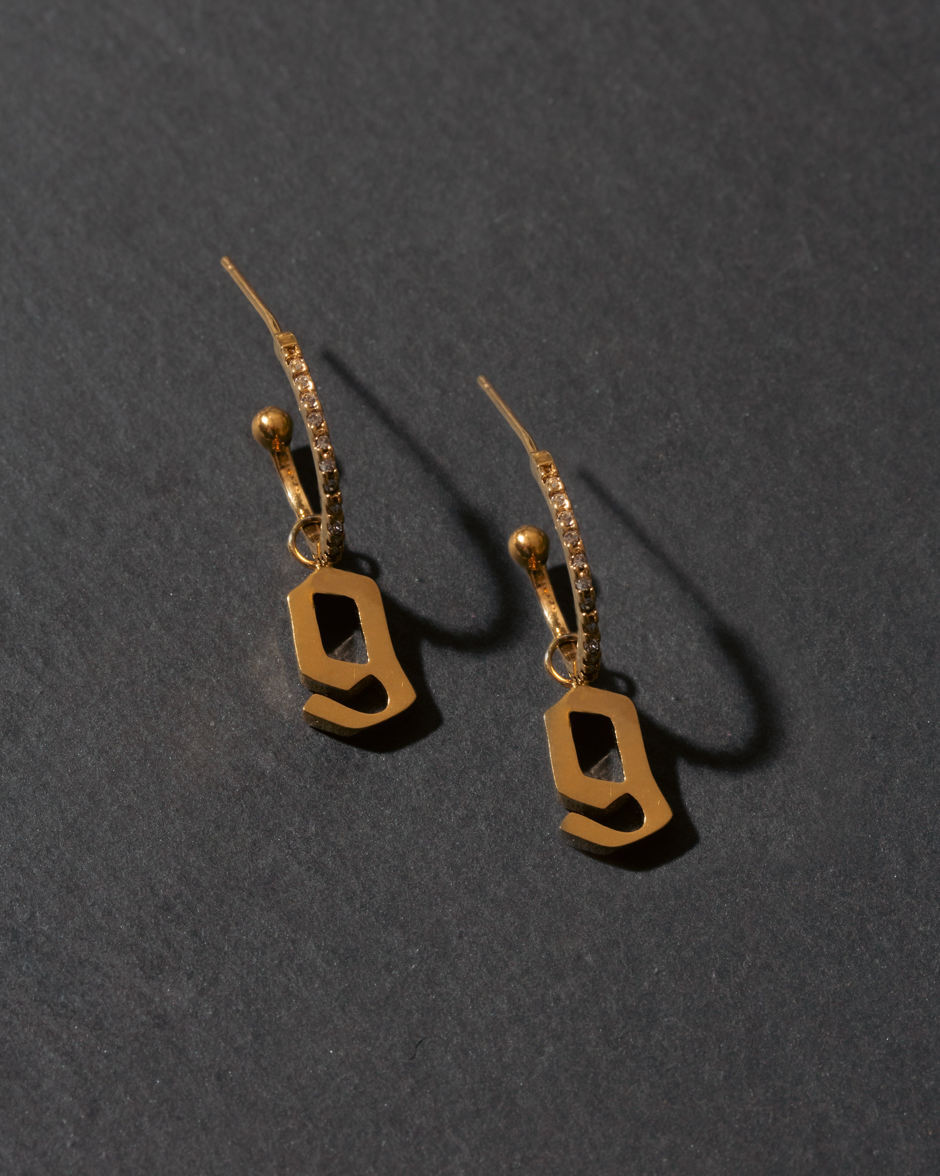 Gold letter 'g' earrings on a dark gray background
