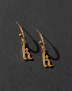 Gold earrings with 'k' letters on a dark gray background