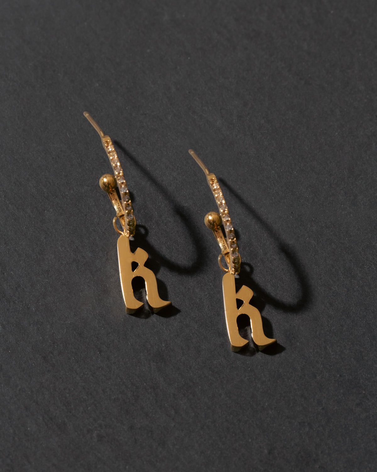 Gold earrings with 'k' letters on a dark gray background