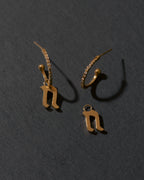 Gold letter 'n' earrings on a dark gray background
