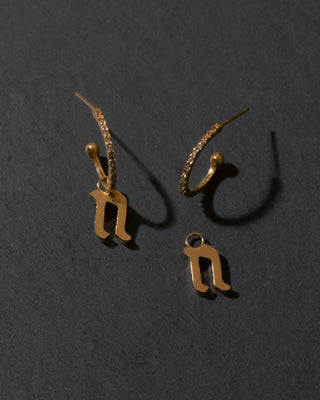 Gold letter 'n' earrings on a dark gray background