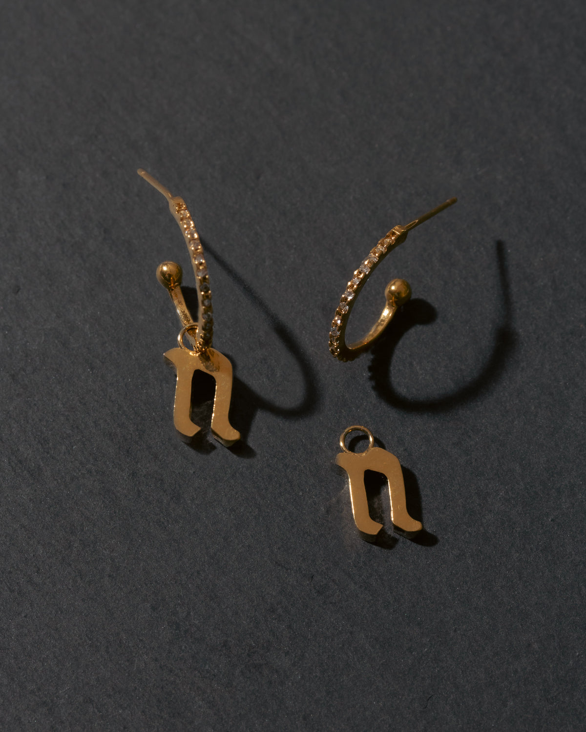 Gold letter 'n' earrings on a dark gray background