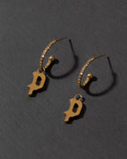 Gold earrings with 'P' charms on a dark gray background