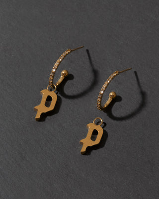 Gold earrings with 'P' charms on a dark gray background