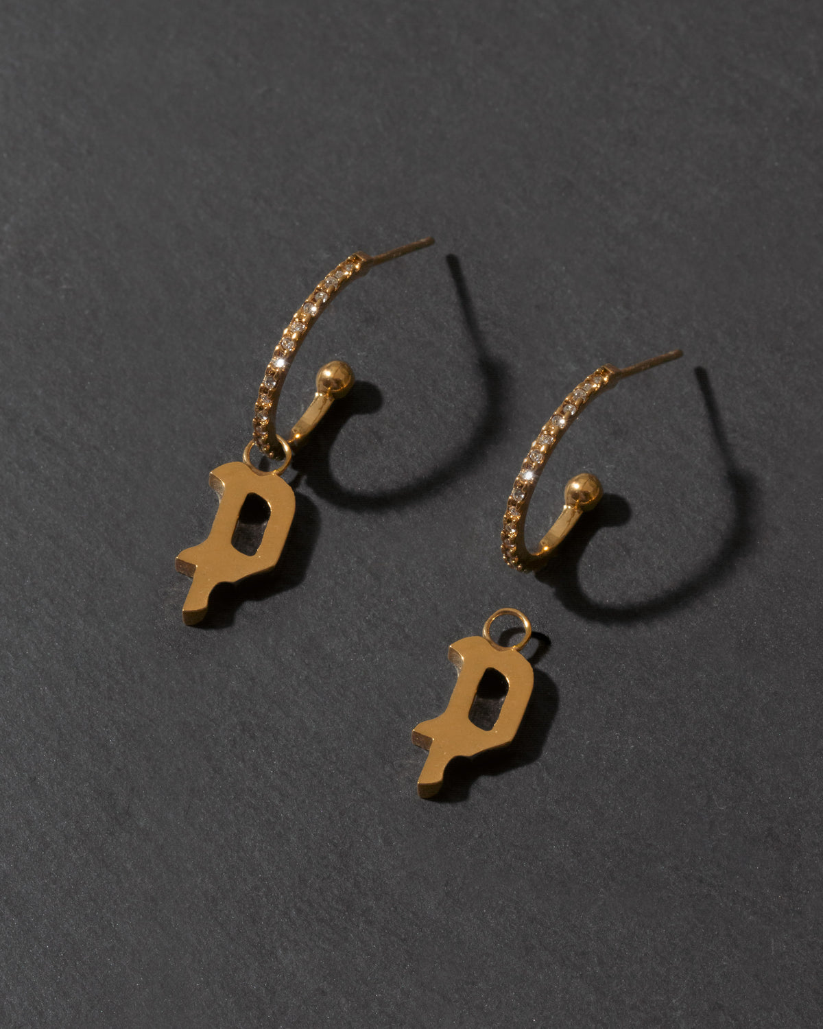 Gold earrings with 'P' charms on a dark gray background