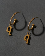 Gold hoop earrings with letter 'q' charms on a dark gray background
