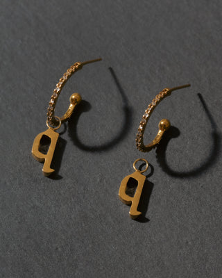 Gold hoop earrings with letter 'q' charms on a dark gray background