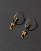 Gold earrings with letter 'R' charms on a dark gray background