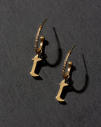 Gold earrings with letter 'T' charms on a dark gray background