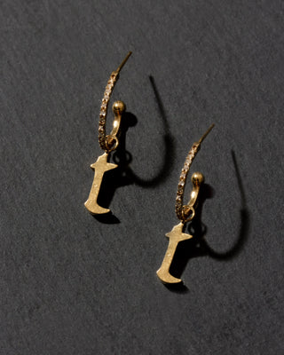 Gold earrings with letter 'T' charms on a dark gray background