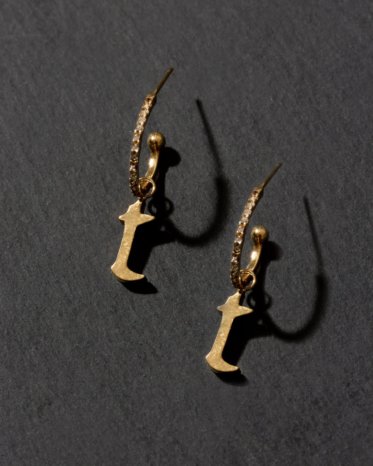 Gold earrings with letter 'T' charms on a dark gray background