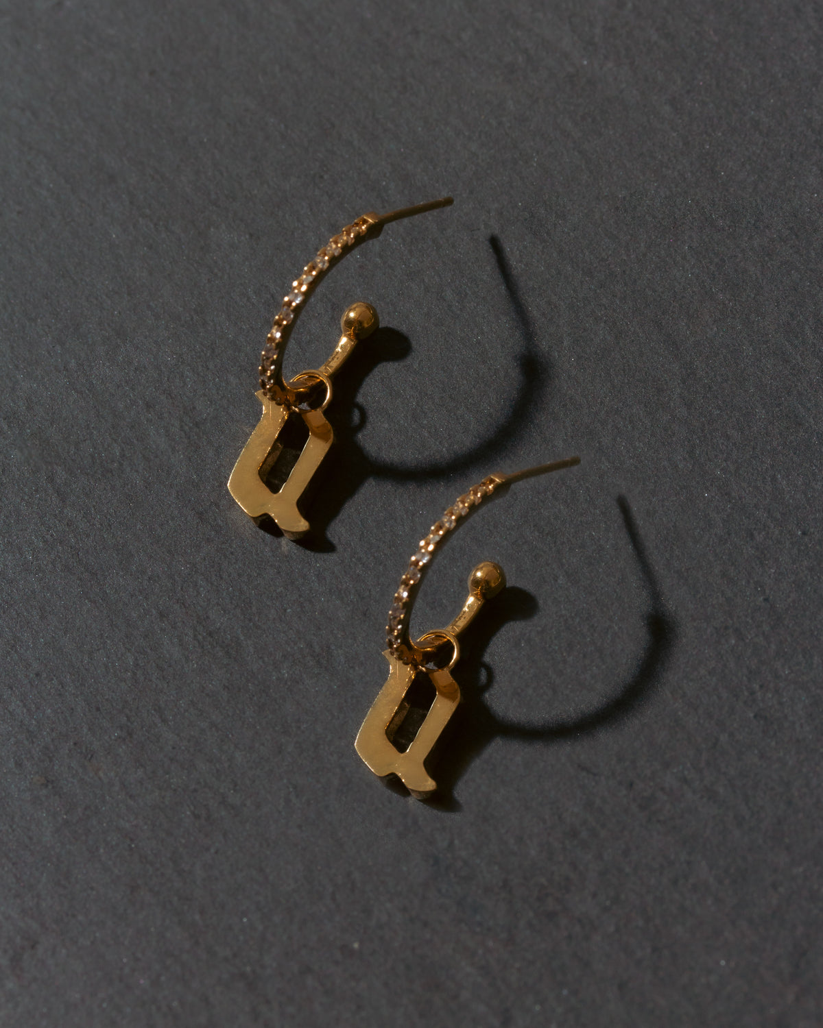 Gold earrings with letter 'u' on a dark gray background