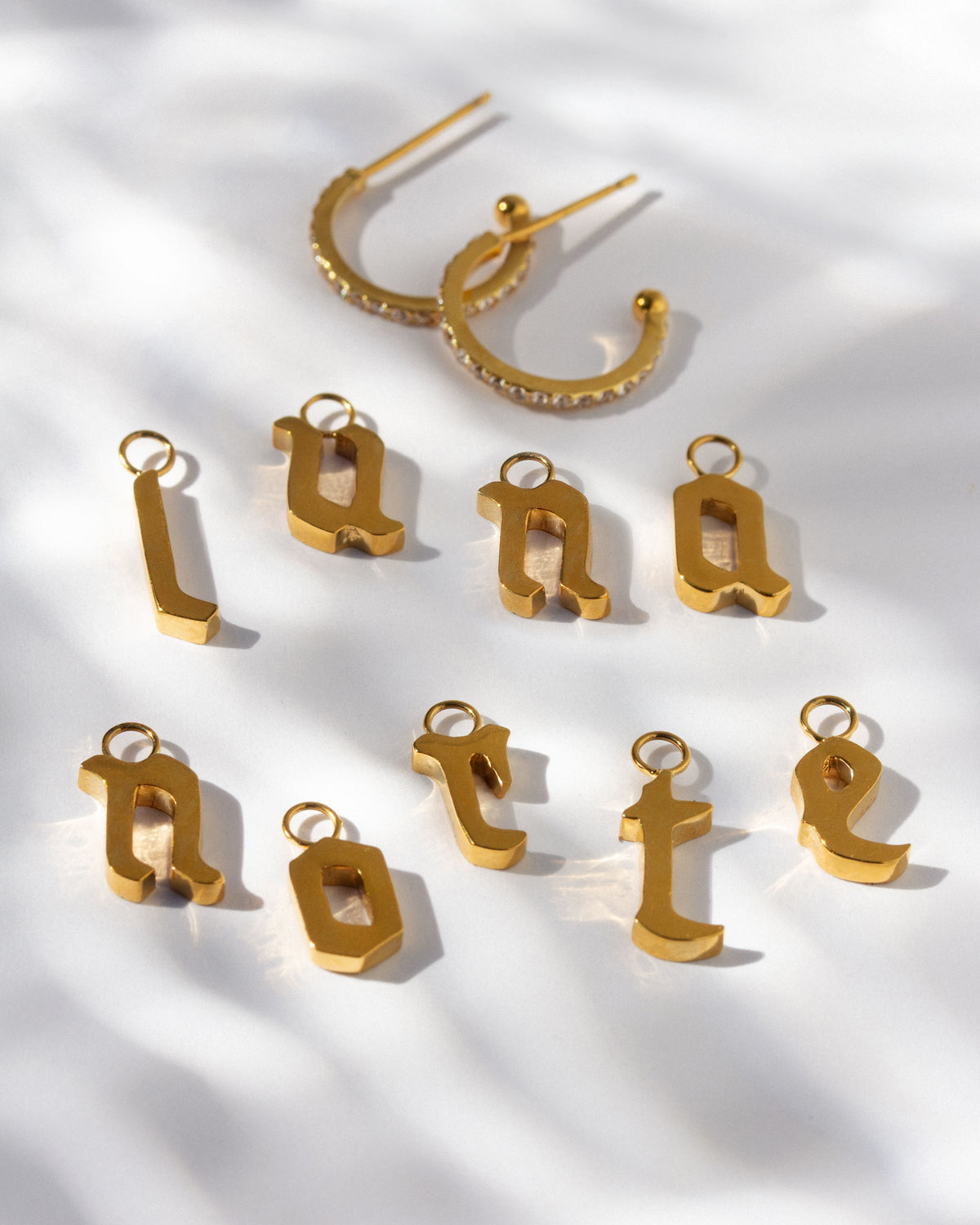 Gold cz earrings pair above many letter-shaped charms spelling out "luna norte." 