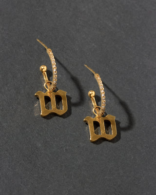 Gold earrings with 'W' charm on a dark gray background