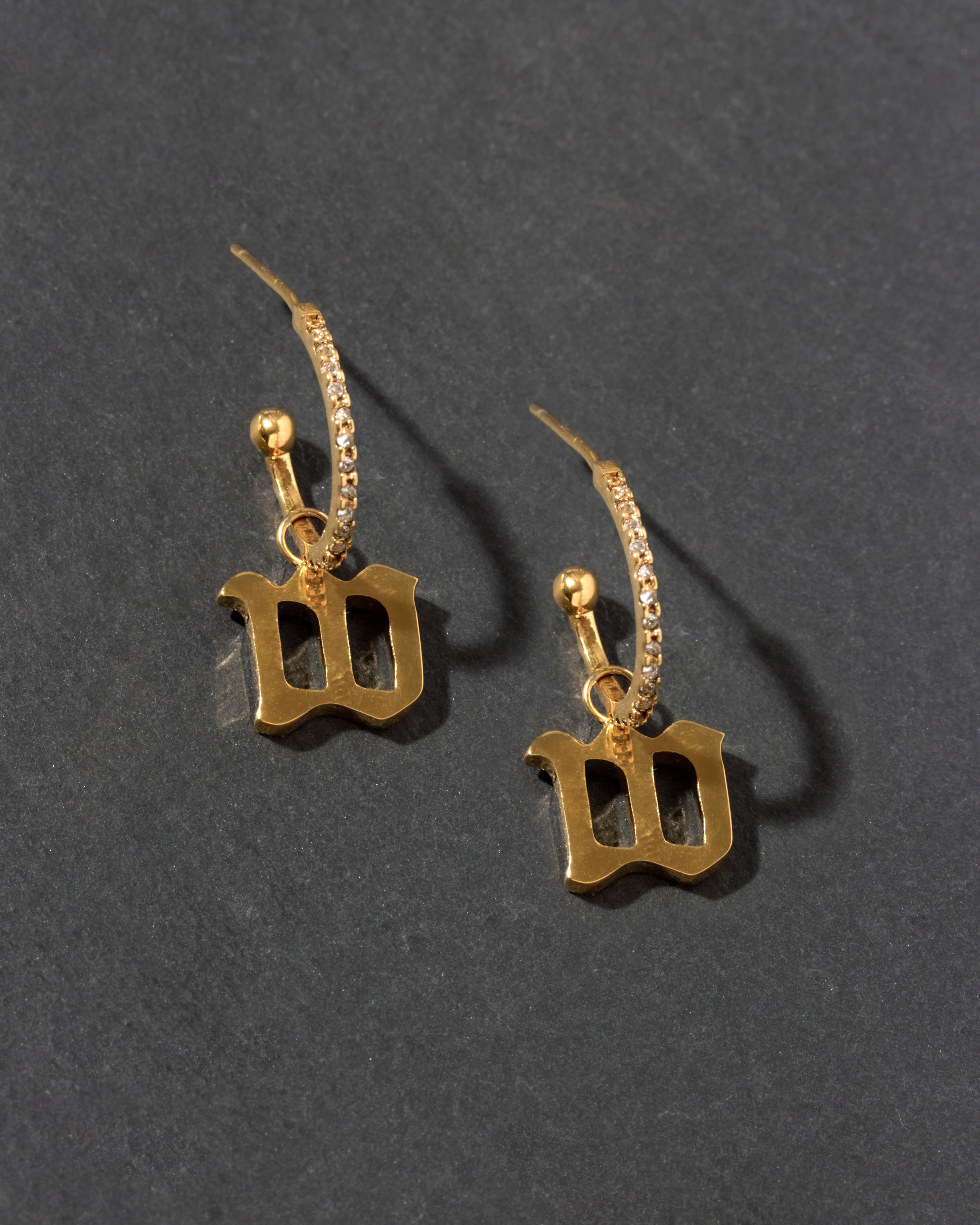 Gold earrings with 'W' charm on a dark gray background