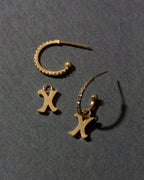 Gold earrings with 'X' charms on a dark gray background
