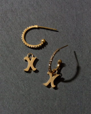 Gold earrings with 'X' charms on a dark gray background