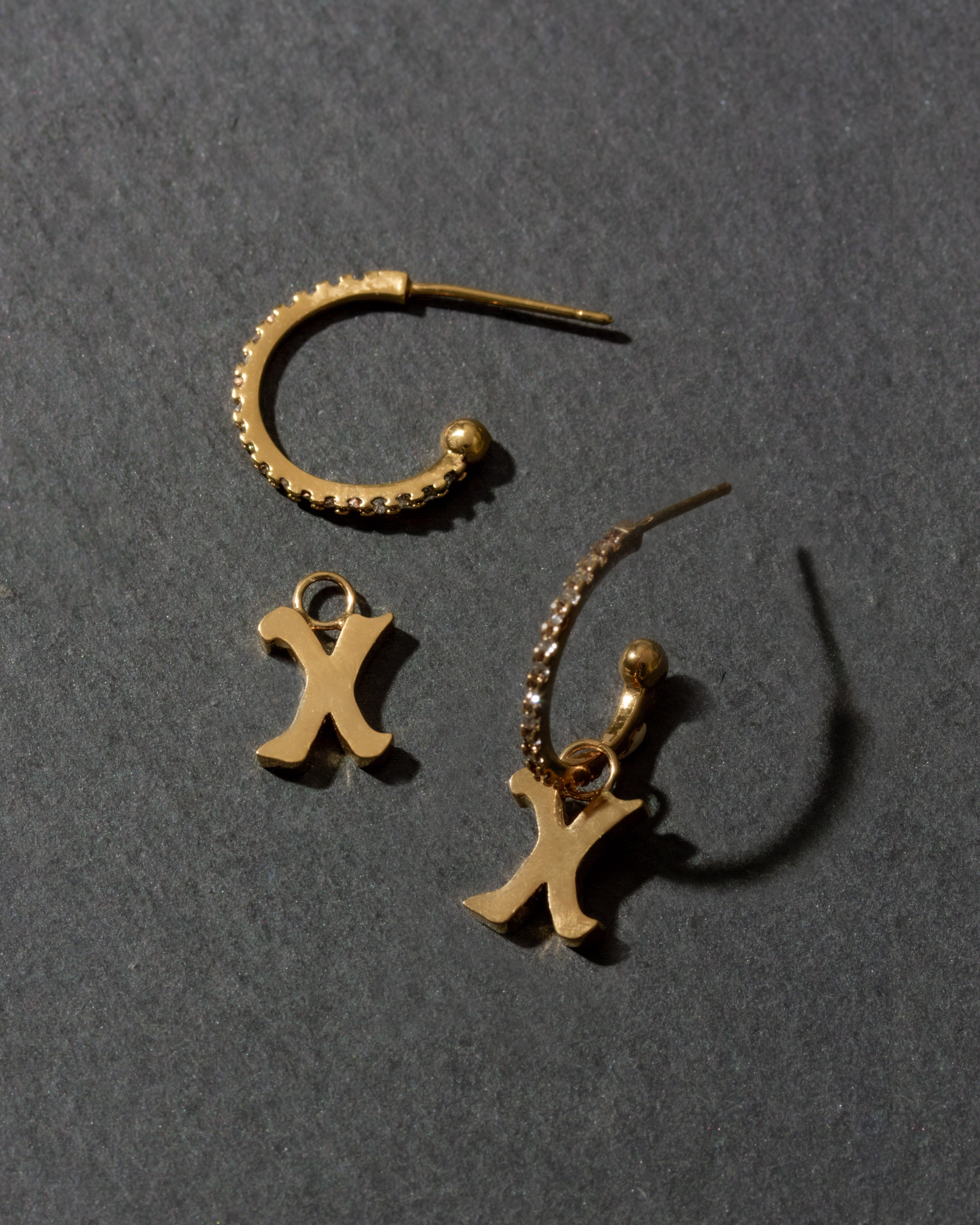 Gold earrings with 'X' charms on a dark gray background