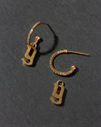 Gold earrings with letter 'y' charms on a dark gray background