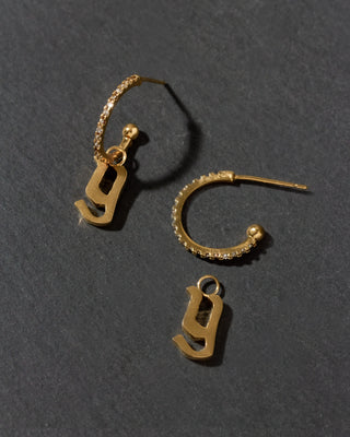 Gold earrings with letter 'y' charms on a dark gray background
