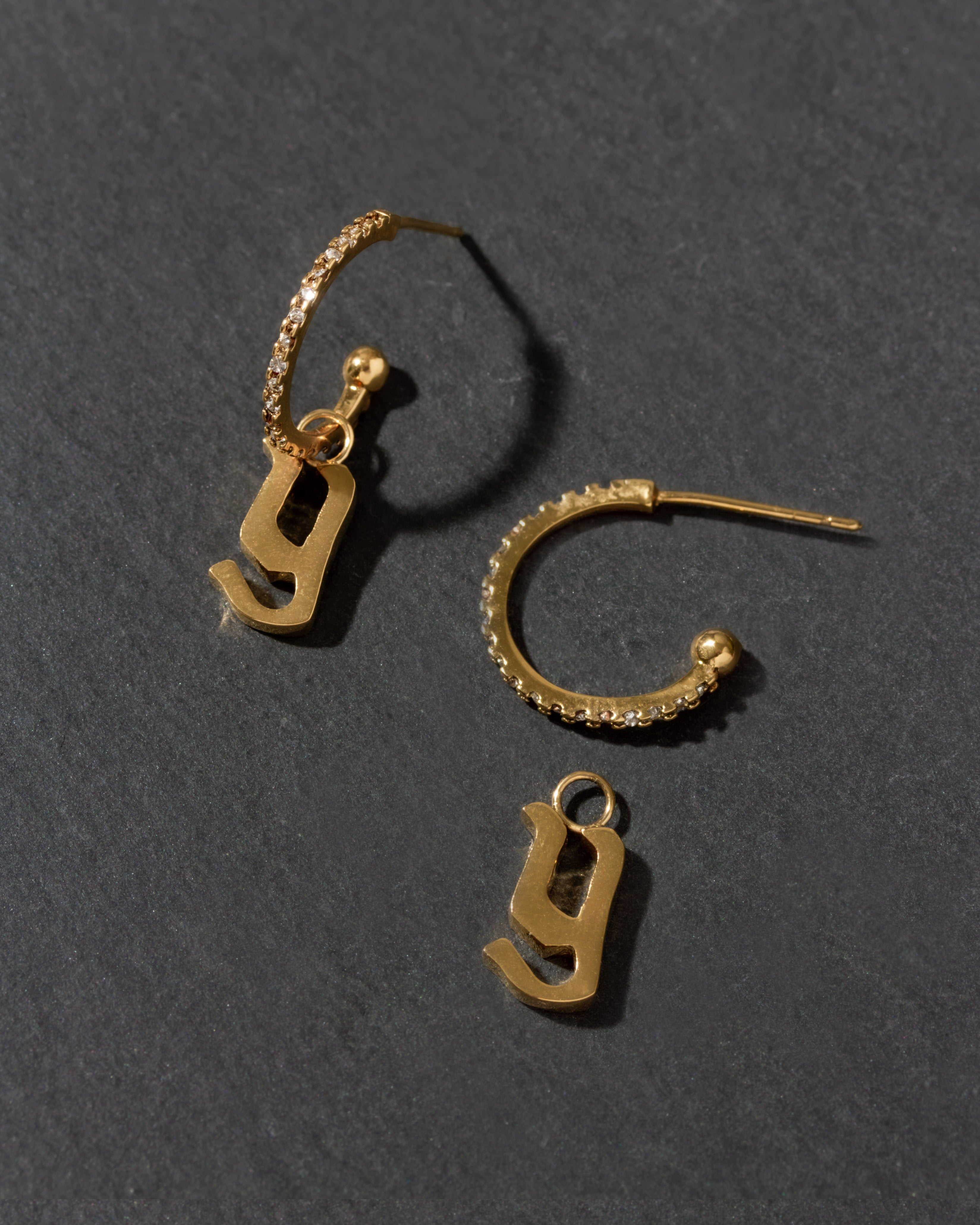 Gold earrings with letter 'y' charms on a dark gray background
