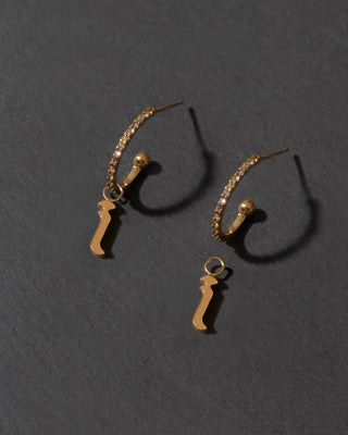 Pair of gold letter "i" earrings on a dark gray background
